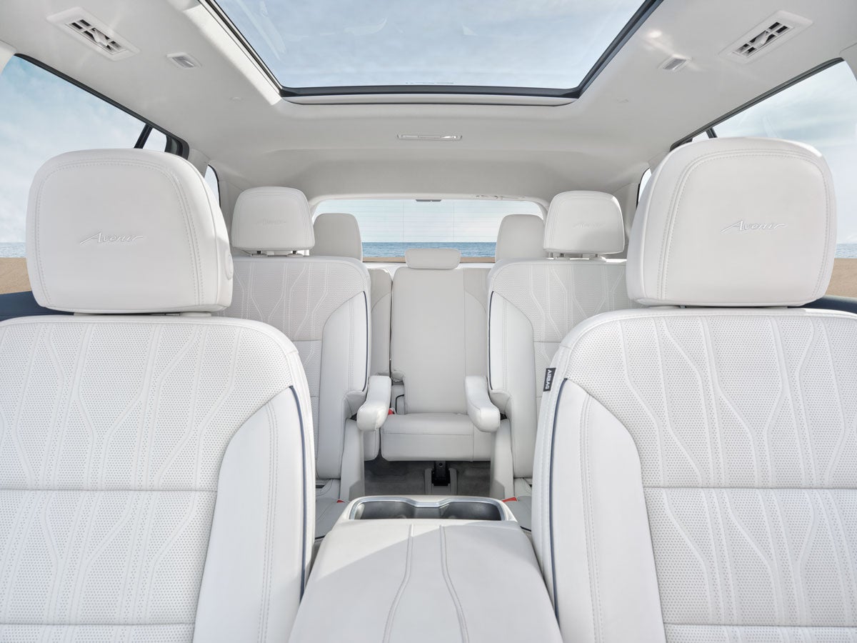 The luxurious interior of a white SUV with three rows of seating, sunroof, and a view of the beach.